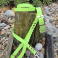The Custom Single Colour Collar in bright green, with a matching lead, is displayed on a weathered wooden post amid rocks and plants outdoors.