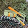 A Bordeaux Grove Extra Wide Collar in green and orange, with a matching lead, is displayed on weathered rope and net outdoors amid greenery—part of the vibrant Bordeaux Grove collection.