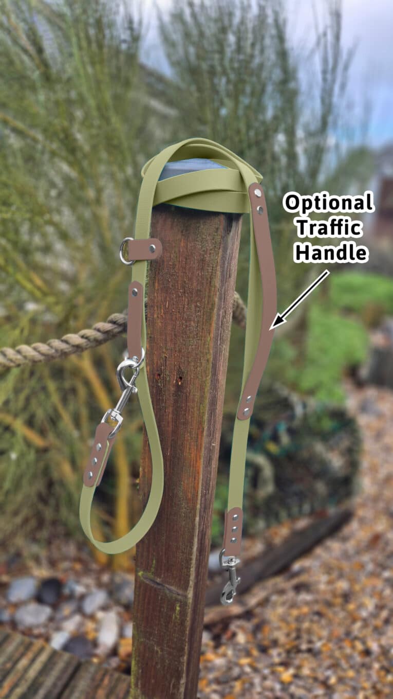 A Custom 2m Multi-way Double-ended Lead with an optional traffic handle is draped over a wooden post outdoors, with greenery and rocks softly blurred in the background. An arrow points to the handle, labelled "Optional Traffic Handle.