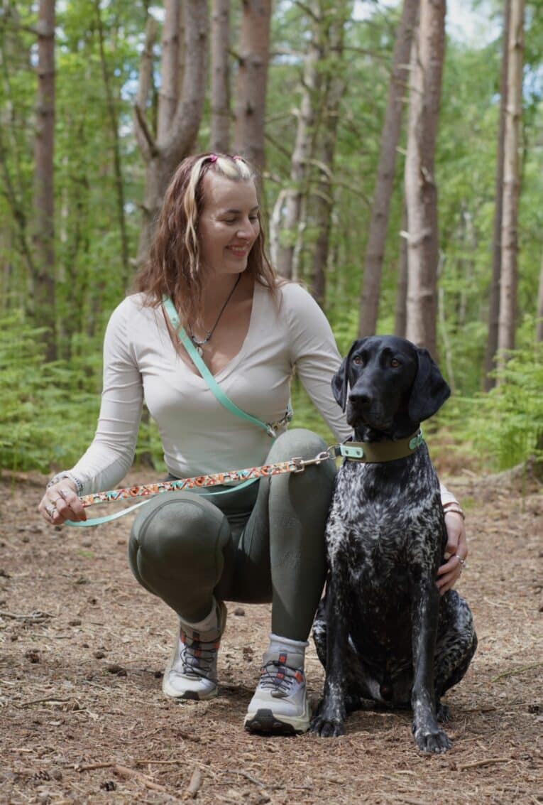 Woman crouching with black and white spotted dog wearing printed accent multiway double-ended lead in woodland setting.
