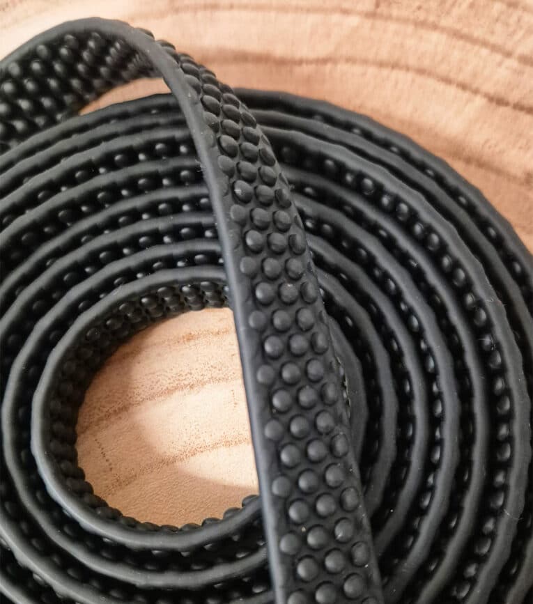 Close-up of a coiled Super-grip Biothane Training Tab / Obedience Lead 51cm with a raised dot pattern, placed on a light wooden surface—perfect for training and obedience sessions.