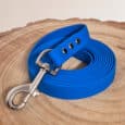 A rolled-up bright blue Waterproof Hexa Long-Line / Training Lead with a metal clasp lies on a round, light wood surface, featuring a subtle hexagonal pattern and three metal-reinforced holes.