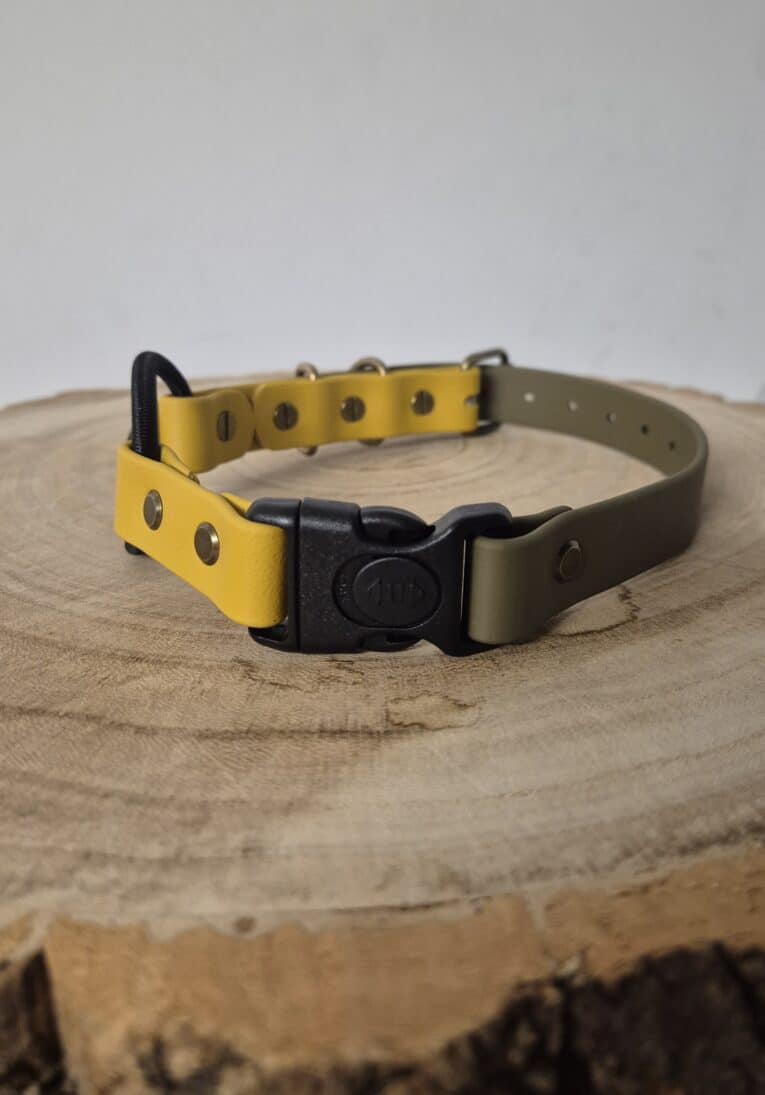 The Quick-Snap Bungee Collar, featuring yellow and olive green colours with a black quick-snap buckle, rests on a round wooden surface displaying visible tree rings.