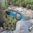 Bright blue and grey quick-snap bungee collar strap displayed on a garden rock, showcasing durable BioThane construction and antique brass hardware.