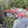 Quick-snap customisable BioThane dog collar strap in coral pink and white, displayed amongst garden plants and stones.