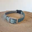 The Custom Quick-Snap Bungee Collar (Copy) features a teal and grey design with a silver buckle and D-ring, shown on a round wooden surface with visible tree rings.