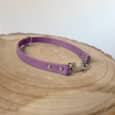 A lavender-coloured dog collar with metal studs and a clasp, displayed on a round wooden surface with visible rings.