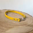 A yellow leather pet collar with metal rivets and a clasp lies on a round wooden surface with visible tree rings, against a plain light background.