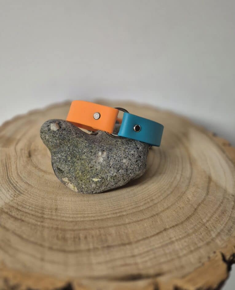 Centre O-Ring Collar in orange and teal Biothane, displayed on a stone and wooden surface, showing the dual-strap design.