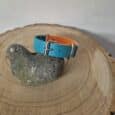 Bright turquoise and orange Biothane Centre O-Ring Collar displayed on wood with stone, showing the distinctive centre O-ring design for safe escape.