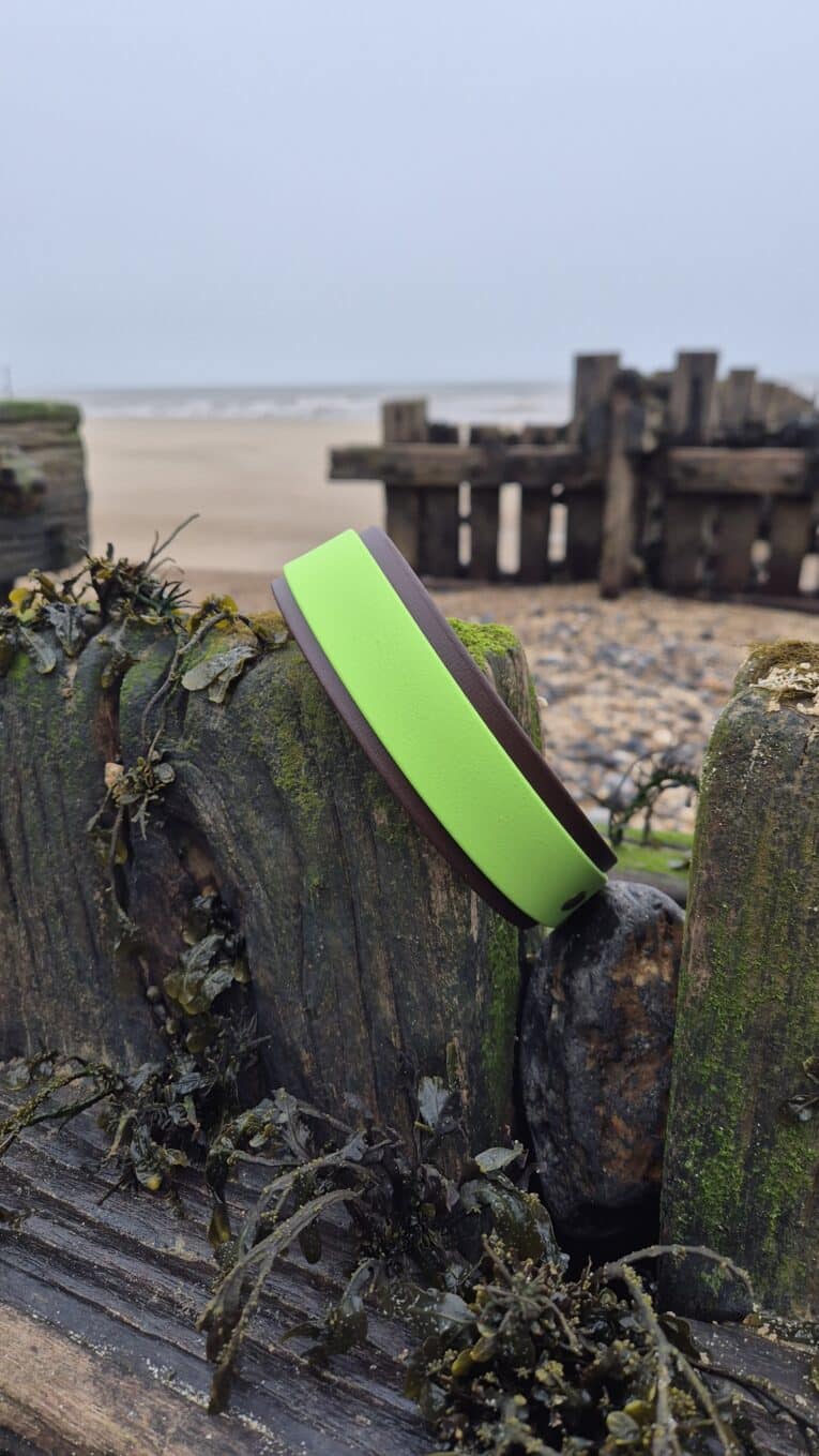 Bright lime-green handmade BioThane dog lead draped over weathered wooden post at coastal beach location.