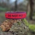 Red Biothane martingale half-slip dog collar with black 'DO NOT PET' text, displayed on textured bark outdoors.
