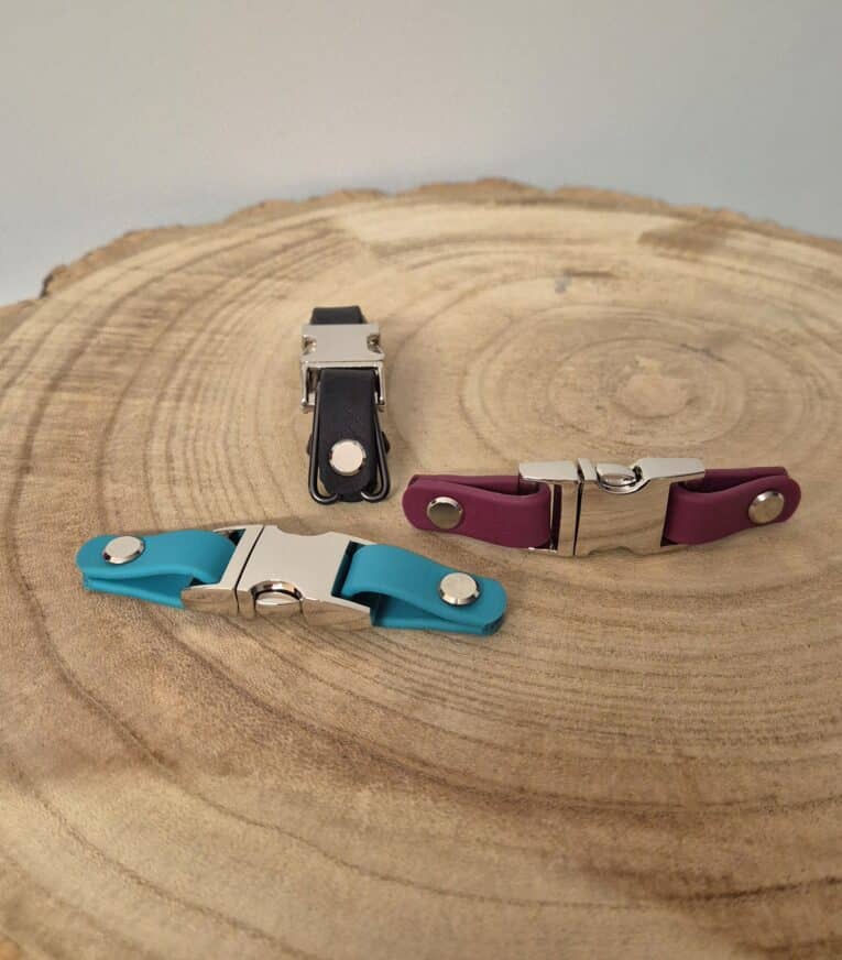 Three handmade BioThane dog collars and leads in turquoise, burgundy, and black displayed on a wooden cross-section.