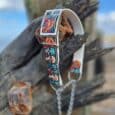 Handmade BioThane dog collar and lead featuring vibrant floral skull embroidery, displayed on weathered wood against blue sky.