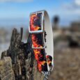 Handmade BioThane dog lead with vibrant flame pattern design, displayed on weathered wood against coastal backdrop.