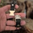 Handmade BioThane dog collar and lead displayed in hand, featuring black and cream hardware against blurred countryside background.