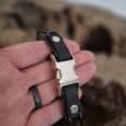 Handmade BioThane dog collar in black and white held in hand, with rugged landscape backdrop.