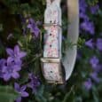 Floral adjustable martingale half-check collar in pink and white, hung among vibrant purple flowers in a garden setting.