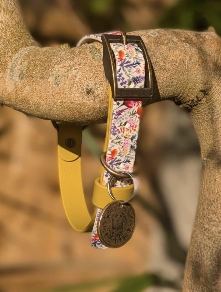 Floral printed BioThane martingale half-slip dog collar with yellow lead and bronze medal charm, draped over a wooden branch.