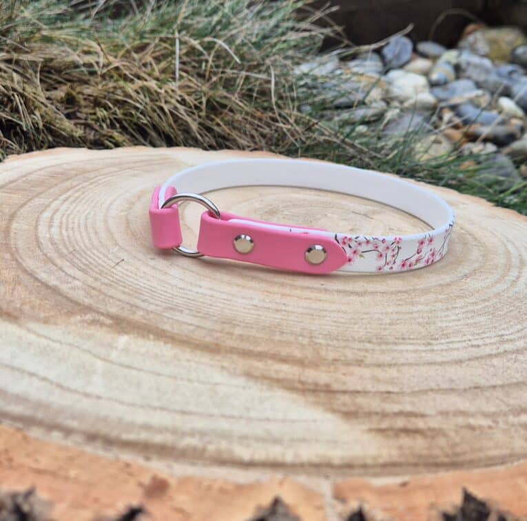 Pink and white floral printed lightweight ID tag collar displayed on natural wood, featuring brass hardware and forward-facing O-ring.