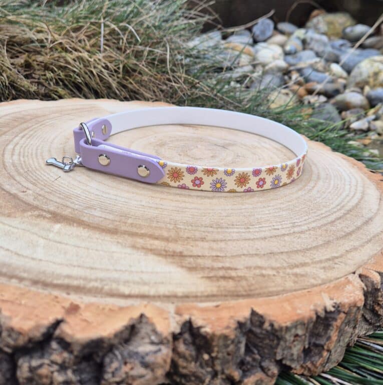 Lavender lightweight ID tag collar with colourful flower print design, displayed on natural wood with brass hardware and forward-facing O-ring.