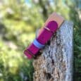 Vibrant magenta and blue double layered hound collar displayed on weathered wood post against blurred garden backdrop.