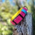 Vibrant custom hound collar in pink, yellow, and blue stacked on weathered wood post outdoors.