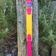 Vibrant custom hound collar in hot pink, yellow and turquoise displayed vertically on weathered wood, showcasing double-layered BioThane construction with brass hardware.