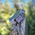 Lavender double-layered hound collar with black buckle displayed on weathered wood post, forest backdrop.