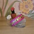 Leopard print double layer dog collar in vibrant magenta and cream, displayed on a glass trinket box with botanical wallpaper background.