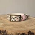 Printed customisable dog collar in cream with pink and sage green abstract pattern, featuring bronze buckle and pink accents on wooden surface.
