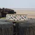 Printed hound collar with pastel leopard pattern displayed on weathered wooden post overlooking beach.