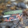 Handmade BioThane dog collars and leads stacked together, featuring vibrant snake and geometric patterns in green, red and white.