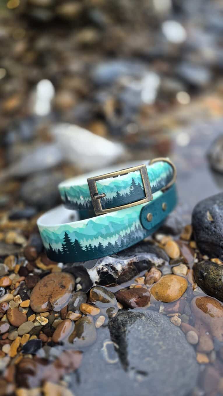 Handmade BioThane dog collar in turquoise with forest tree design, displayed on coastal pebbles and rocks.