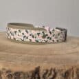 Printed hound collar with leopard spot pattern in pink, black and cream, featuring waterproof Biothane construction and antique brass hardware on wooden surface.