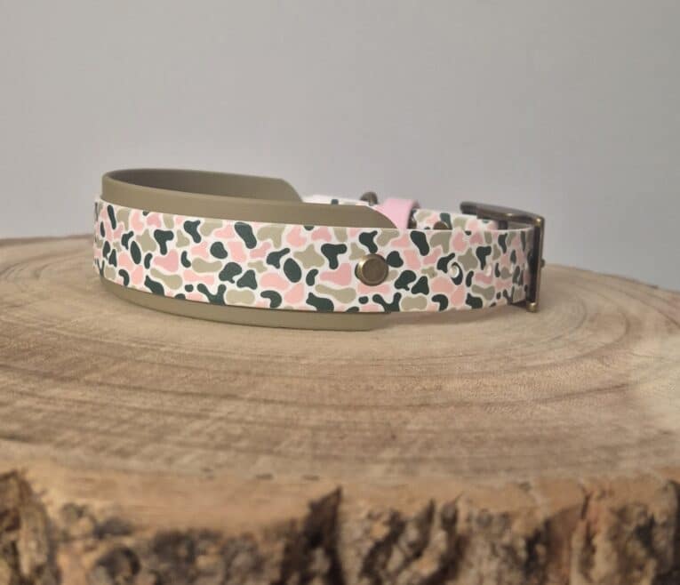 Printed hound collar with leopard spot pattern in pink, black and cream, featuring waterproof Biothane construction and antique brass hardware on wooden surface.
