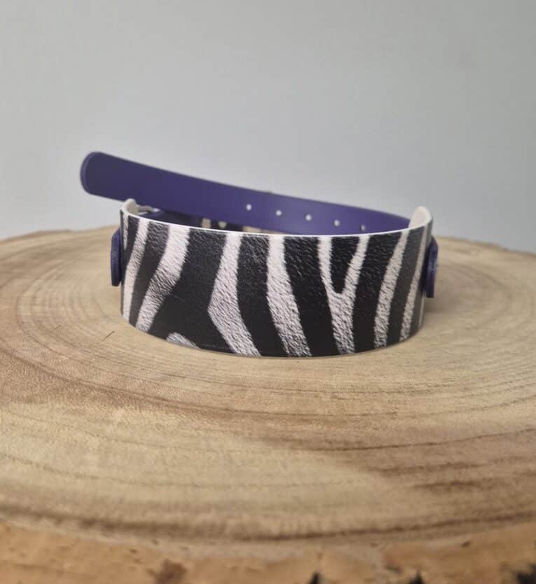 Zebra-striped printed Biothane dog collar with navy blue quick-snap hardware, displayed on natural wooden surface.