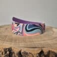 Colourful printed dog collar with swirling abstract design in coral, purple, and blue tones, displayed on wooden surface.