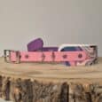 Pink waterproof BioThane dog collar with quick-snap hardware displayed alongside purple and patterned printed hound collar options on wooden surface.