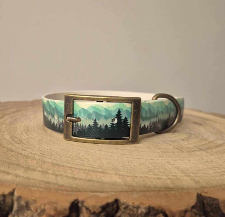 Handmade BioThane dog collar featuring a mountain forest landscape design with teal and charcoal tones, displayed on natural wood.