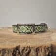 Handmade BioThane dog collar in lime green and black snake pattern, displayed on natural wood with polished metal buckle.