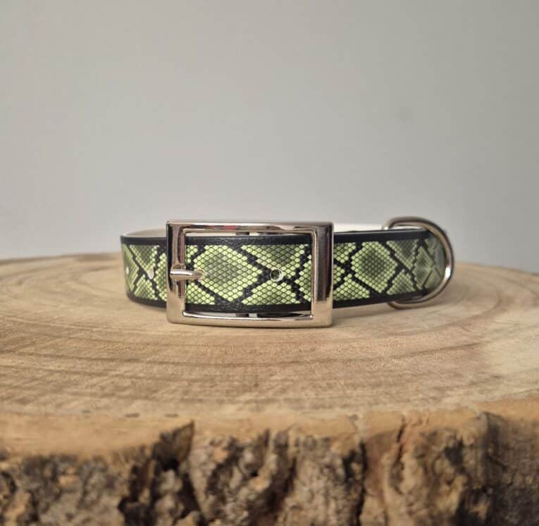 Handmade BioThane dog collar in lime green and black snake pattern, displayed on natural wood with polished metal buckle.