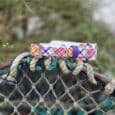 Colorful printed quick-snap dog collar featuring blue, red, and yellow geometric pattern, displayed on weathered rope with lichen.
