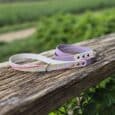 Two printed hound collars in white and lavender, displayed on a wooden rail overlooking green fields, showcasing vibrant geometric patterns and quality hardware.