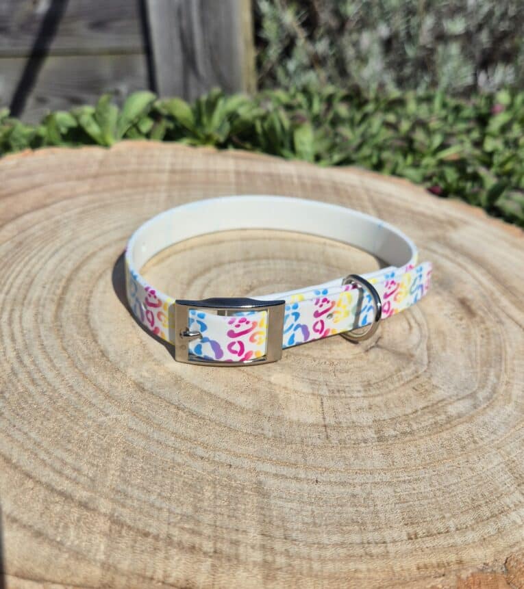 Colourful handmade BioThane dog collar with pink, blue and yellow pattern, displayed on wooden surface with garden background.