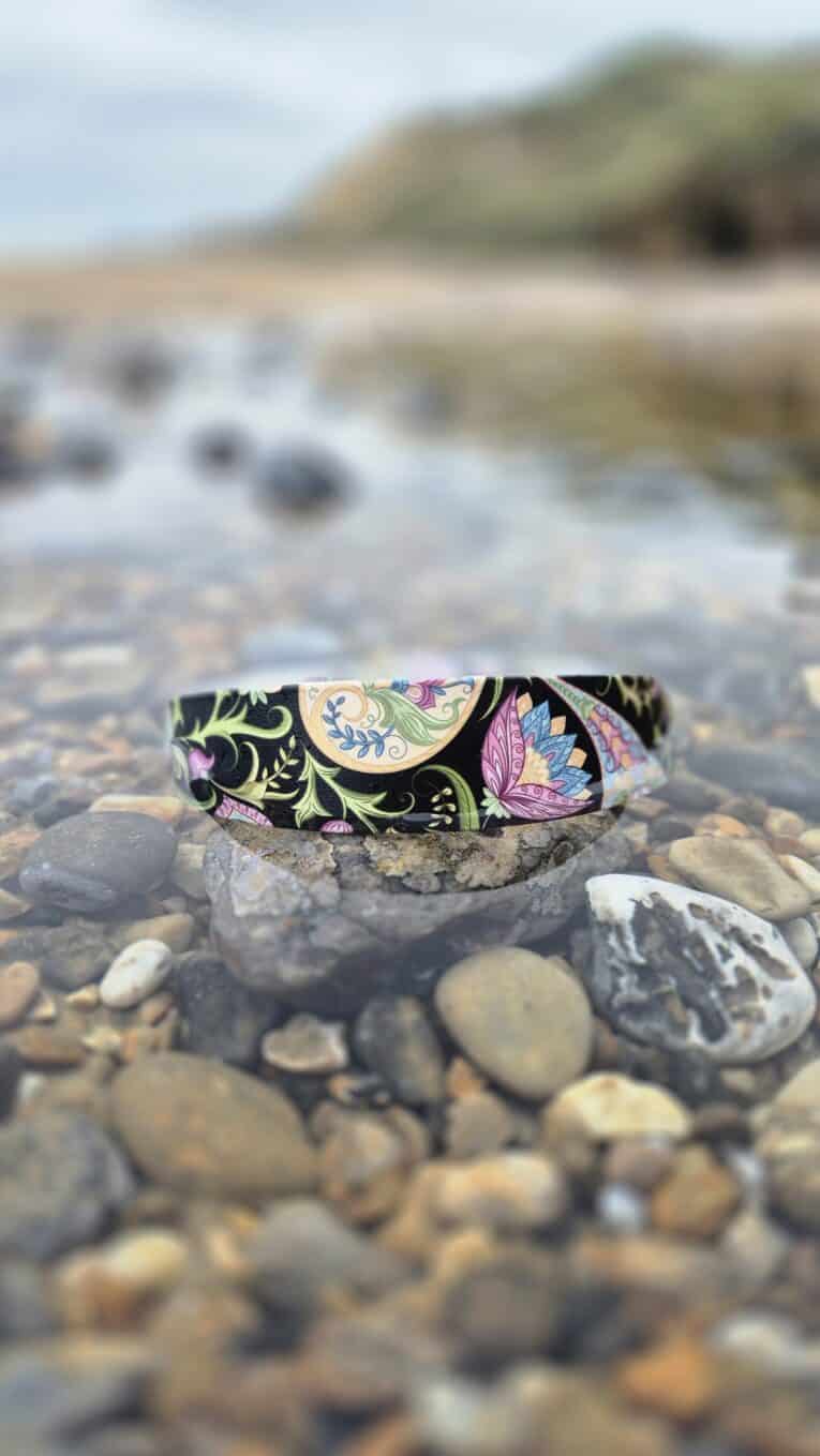 Colourful quick-snap customisable dog collar with botanical print design positioned on pebbles by the shore, showcasing waterproof durability.