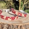 Red printed dog collar with gingerbread man design displayed on wooden surface with white hardware and festive styling.