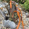 Handmade BioThane double-ended lead set in orange and brown with brass fittings, displayed on coastal pebbles.