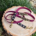 Handmade BioThane dog collars and multiway lead in berry and blackwood colours with gold hardware, displayed on wood.
