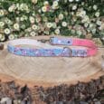 Handmade BioThane dog lead with blue floral print and pink reverse, displayed on wooden log amongst daisies.